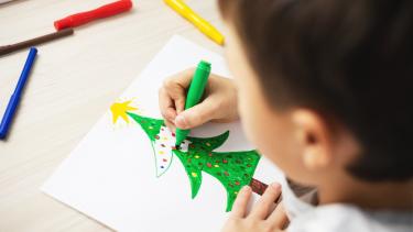 Child drawing Christmas tree on paper with felts